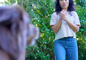 Woman appearing fearful as a dog approaches, illustrating the anxiety and distress associated with cynophobia